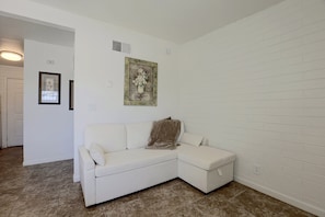 Um sofá branco em forma de L numa sala com parede de tijolos brancos e chão em azulejos.