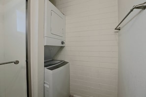 Uma lavanderia com máquina de lavar e secadora, uma porta e uma parede de tijolos.