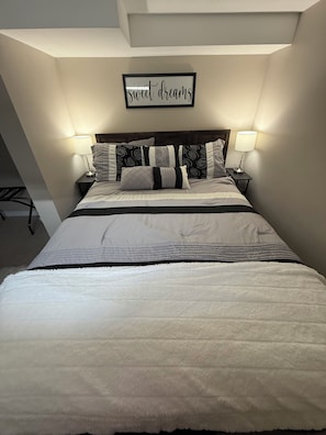 Una cama bien tendida con cabecera, dos mesitas de noche con lámparas, y un cartel en la pared que dice 'sweet dreams'.