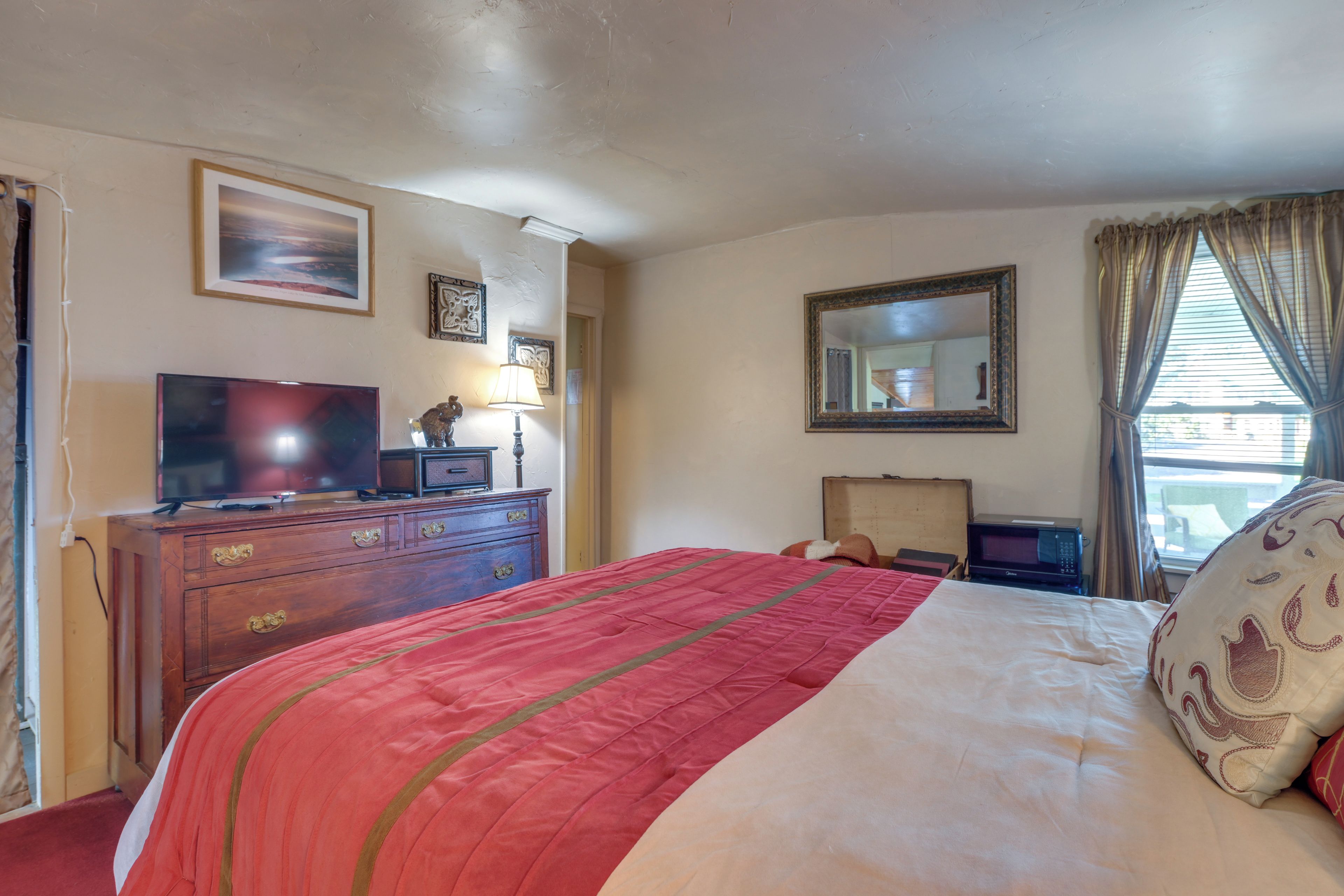 A hotel room with a bed, a dresser, a television, a lamp, and a window with curtains.