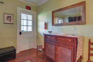 Une pièce avec une porte blanche portant l’inscription « SORTIE », un meuble en bois avec des tiroirs, un miroir et un petit tabouret.