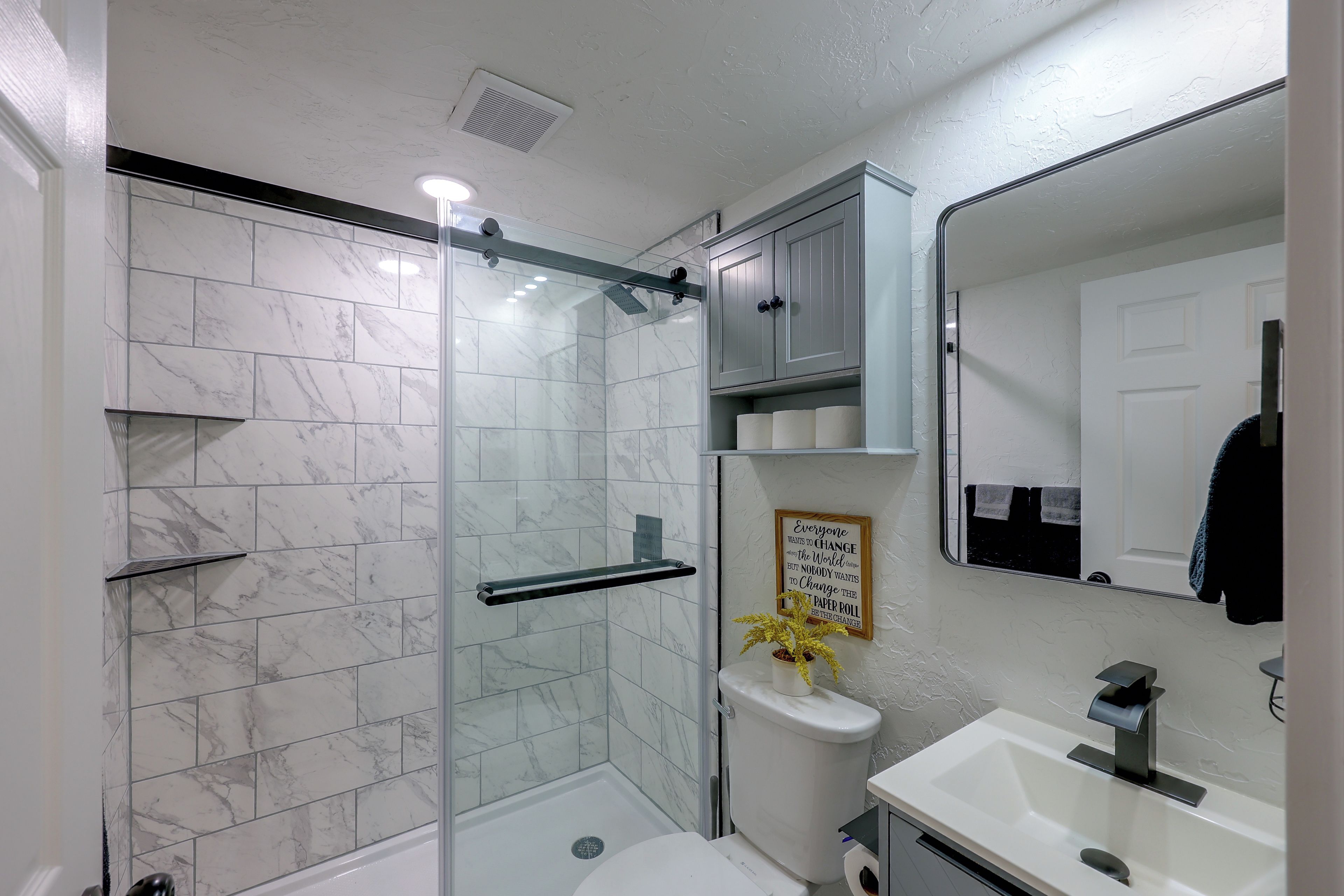 Un baño con cabina de ducha de vidrio, un lavabo blanco y un espejo.