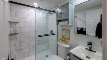 Un baño con cabina de ducha de vidrio, un lavabo blanco y un espejo.