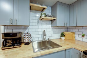 Una cocina con armarios azul claro, un lavamanos de acero inoxidable, una cafetera y una encimera de madera.