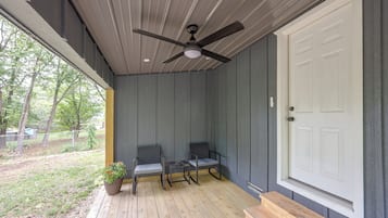 A covered porch with a ceiling fan, two chairs, a small table, and a potted plant.