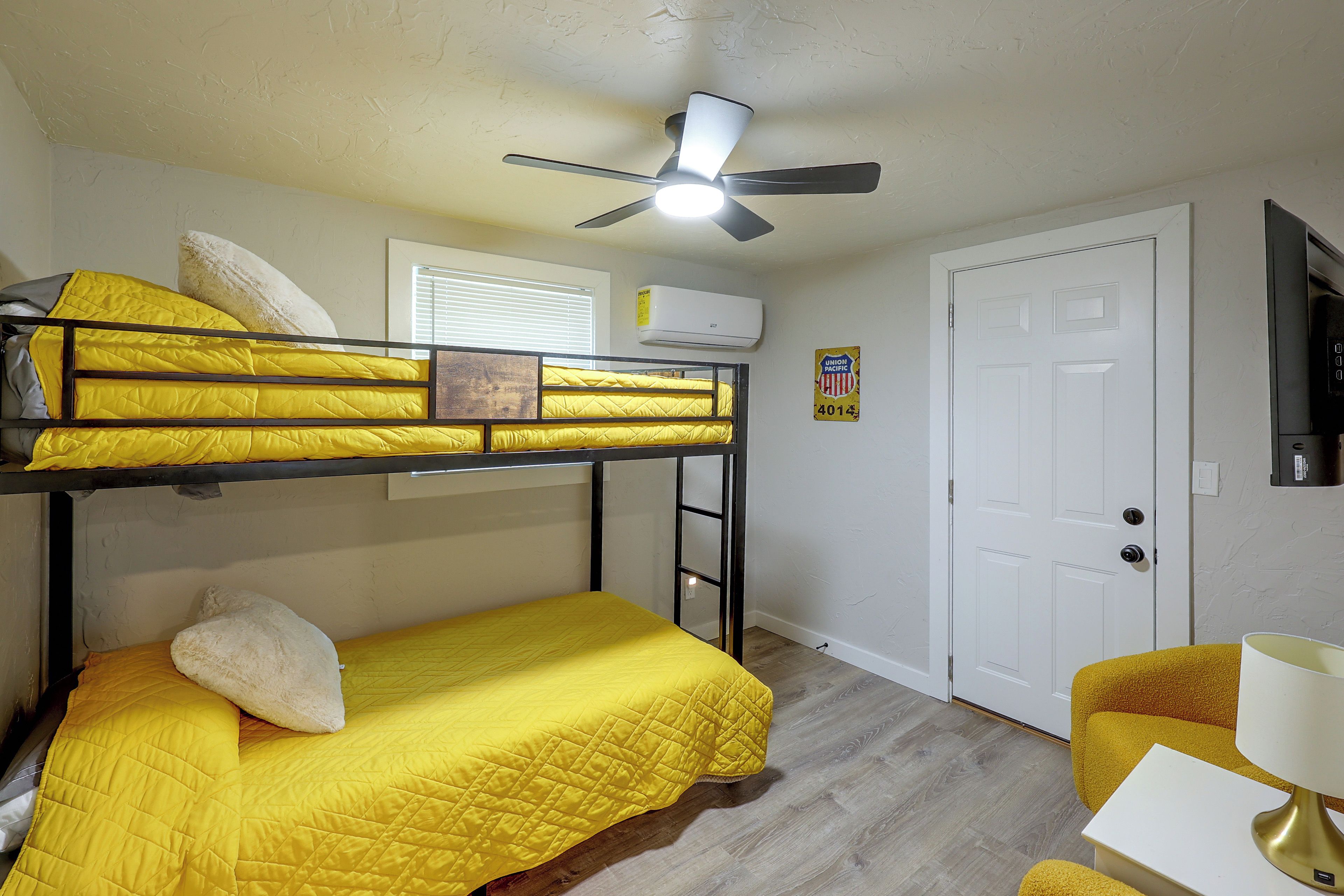 A bunk bed room with a ceiling fan, a white door, and a small table with a lamp.