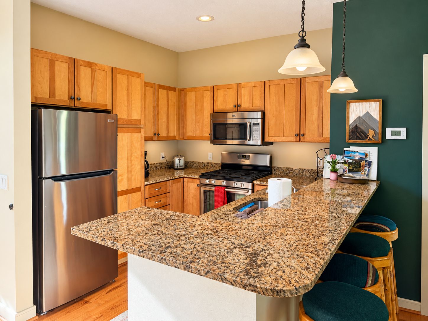 A kitchen with wooden cabinets, stainless steel appliances, granite countertops, and bar stools.