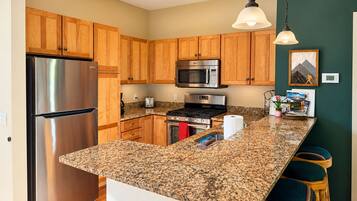 A kitchen with wooden cabinets, stainless steel appliances, granite countertops, and bar stools.