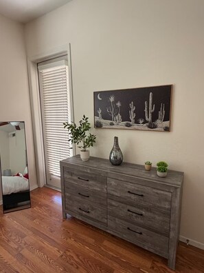 A room with a wooden dresser, a mirror, a cactus painting, and a door with blinds. - Fun in the Sun, Baseball, Luxury Condo! (Surprise)