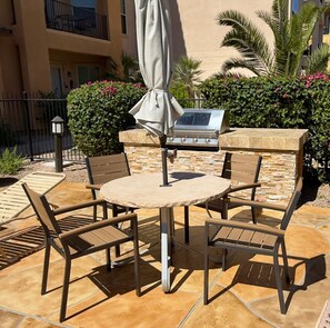 An outdoor patio with a round table, four chairs, a grill, and a covered umbrella. - Fun in the Sun, Baseball, Luxury Condo! (Surprise)
