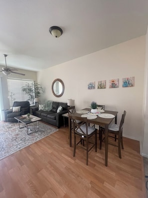 A living room with a dining table, chairs, a sofa, a coffee table, a ceiling fan, and wall art. - Fun in the Sun, Baseball, Luxury Condo! (Surprise)