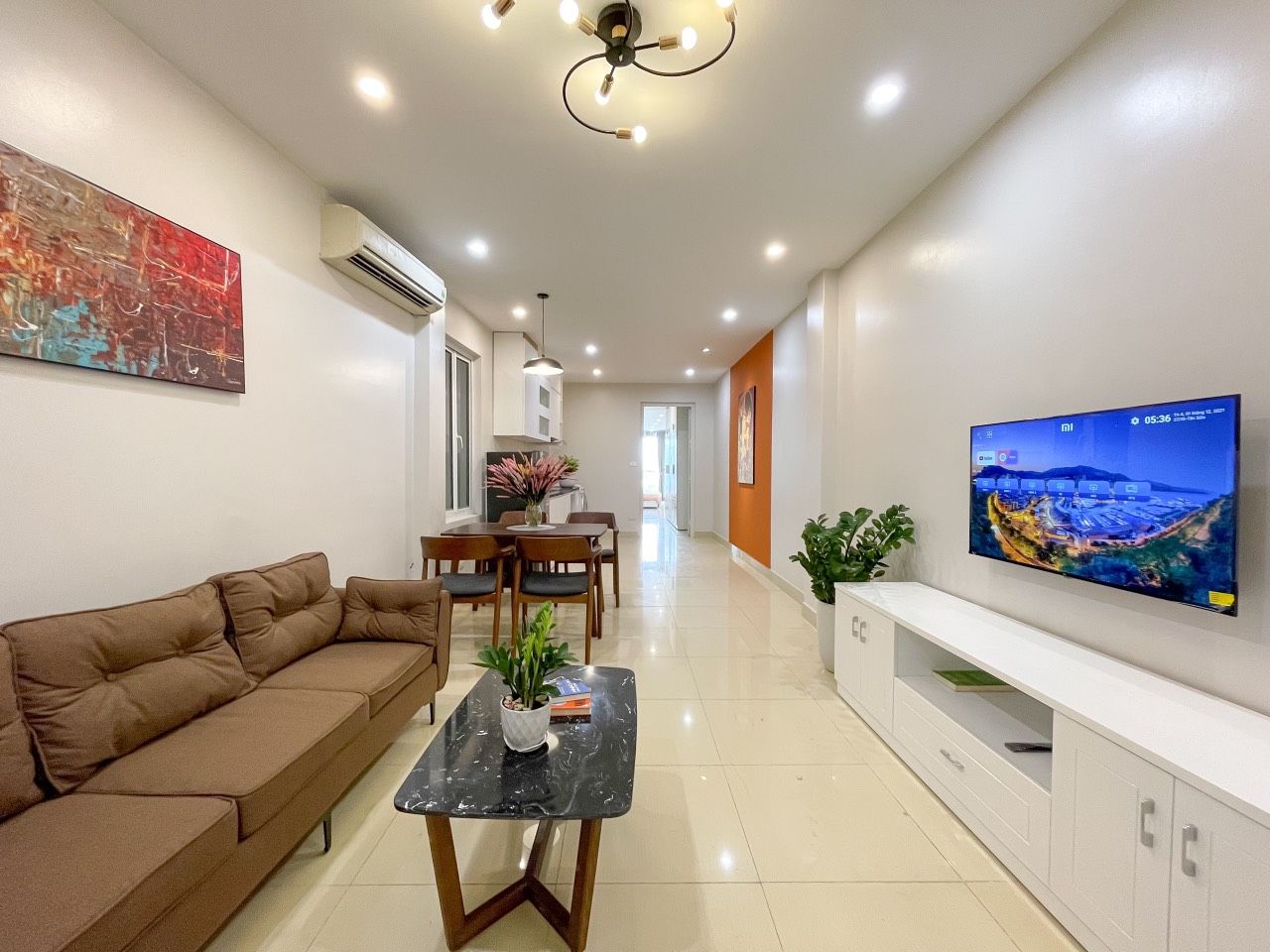 A modern living room with a sofa, a coffee table, a TV, and a dining area with chairs and a table.