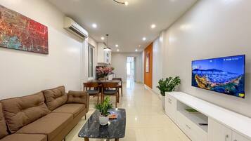 A modern living room with a sofa, a coffee table, a TV, and a dining area with chairs and a table.