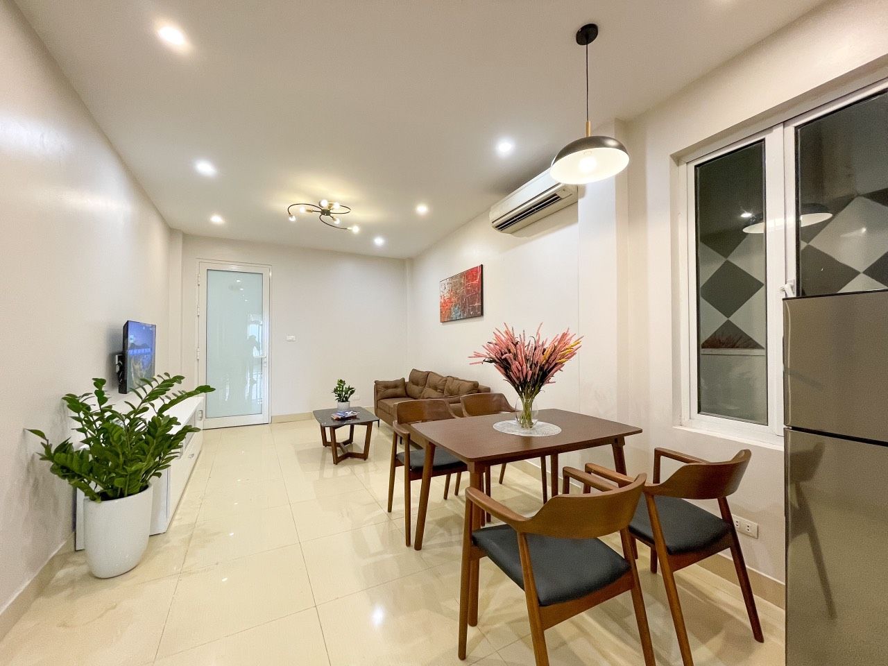 A modern kitchen with a refrigerator, a dining table with chairs, and a potted plant.
