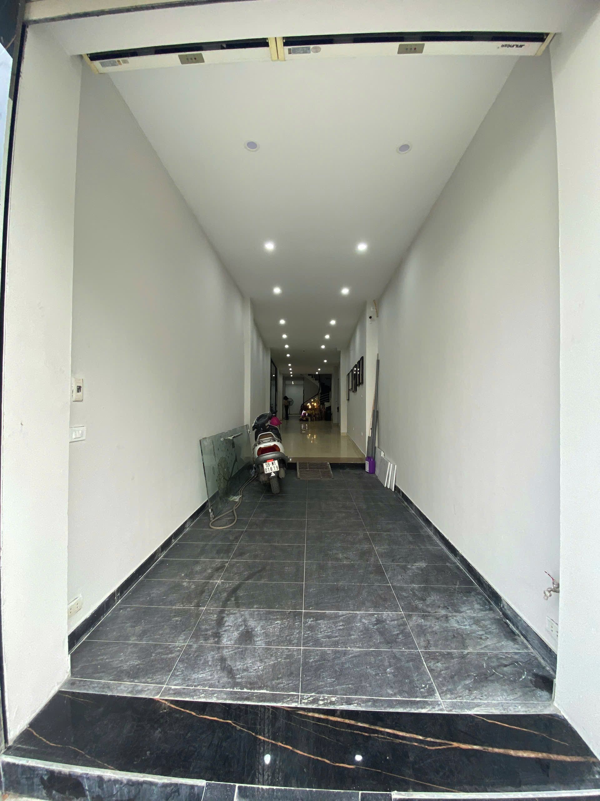 A corridor with a scooter parked, leading to a staircase and a room with a bed.