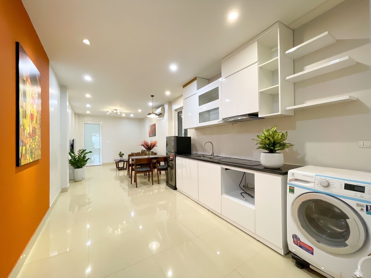 A modern kitchen with white cabinets, a built-in washing machine, and a dining area with a table and chairs.