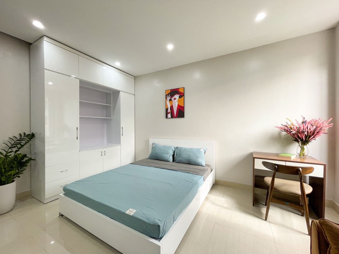 A bedroom with a bed, a desk, a chair, a wardrobe, and a potted plant.
