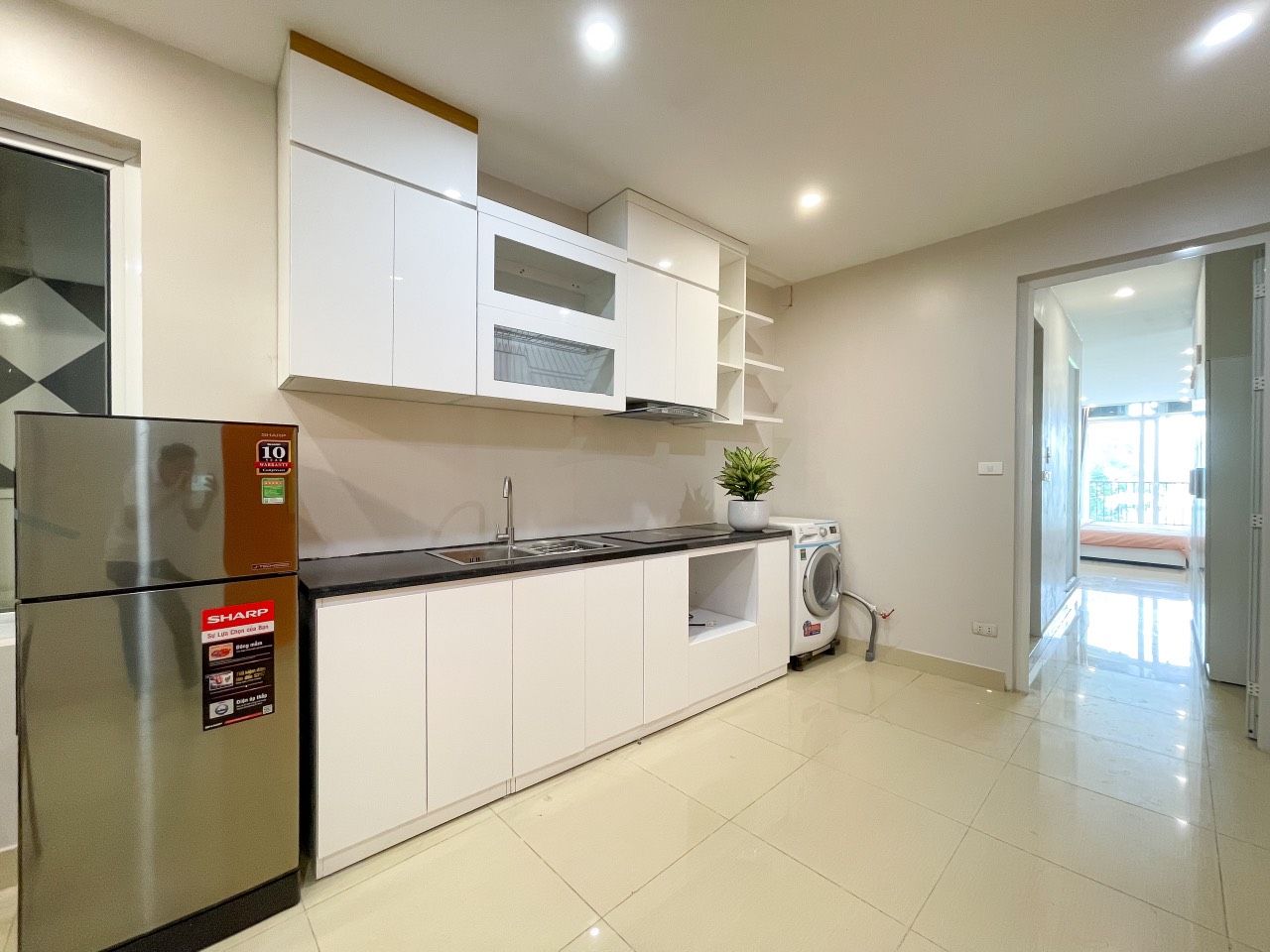 A modern kitchen with white cabinets, a stainless steel refrigerator, a washing machine, and a sink.