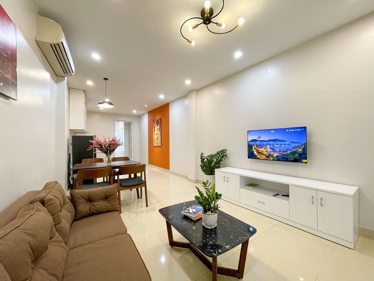 Una sala moderna con sofá, mesa de comedor, televisor y un armario blanco.