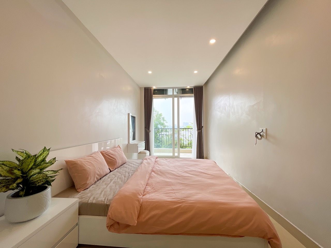A bedroom with a bed, a nightstand, a potted plant, and a window with curtains.