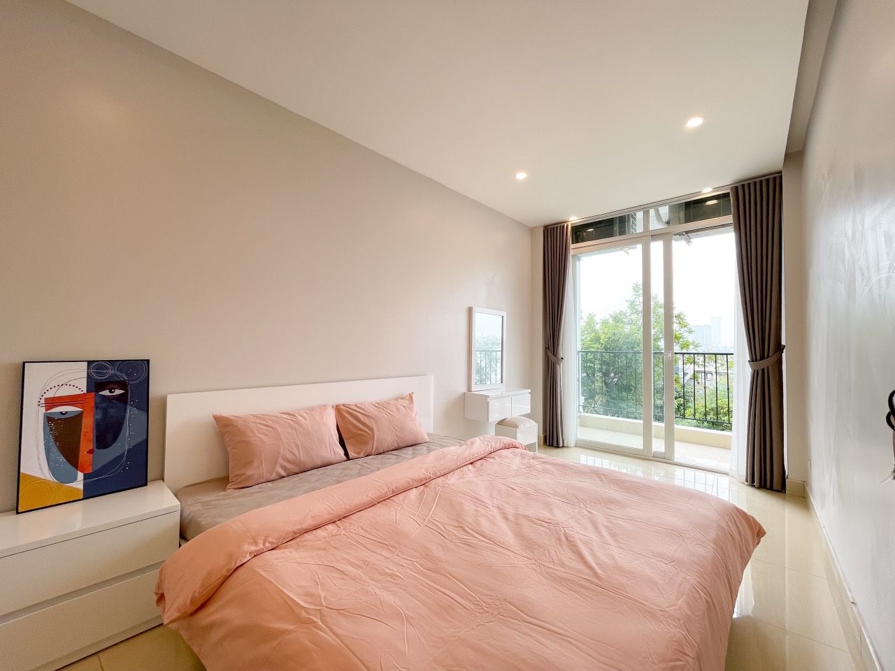 A modern bedroom with a large bed, a nightstand, a painting, and a balcony with curtains.