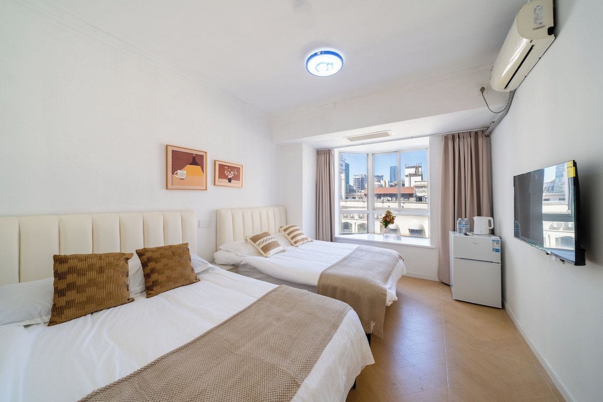 Quarto de hotel com duas camas, televisão de tela plana, minibar e uma janela grande com vista para a cidade.