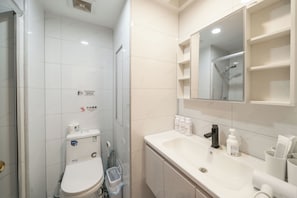 Casa de banho com sanita, chuveiro e lavatório com artigos de higiene pessoal.