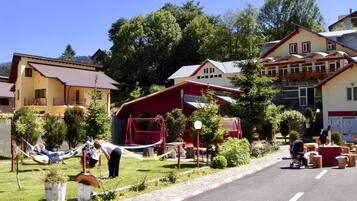 Un hotel con un edificio de techo rojo, un área verde con una hamaca y un camino pavimentado.