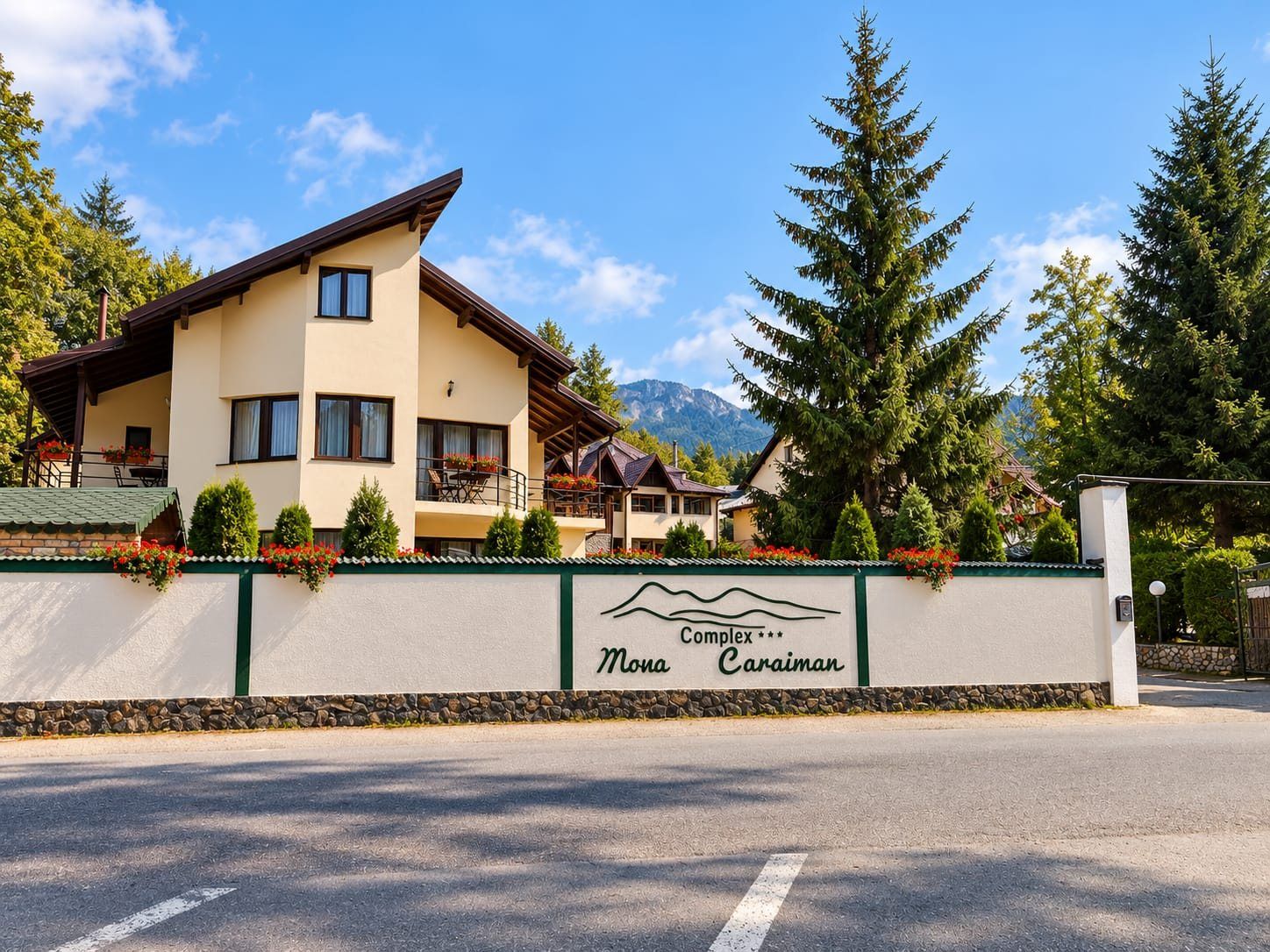 A hotel with a mountain view, a sign indicating 'Complex' and 'Mona Caraman,' and a paved road in front.