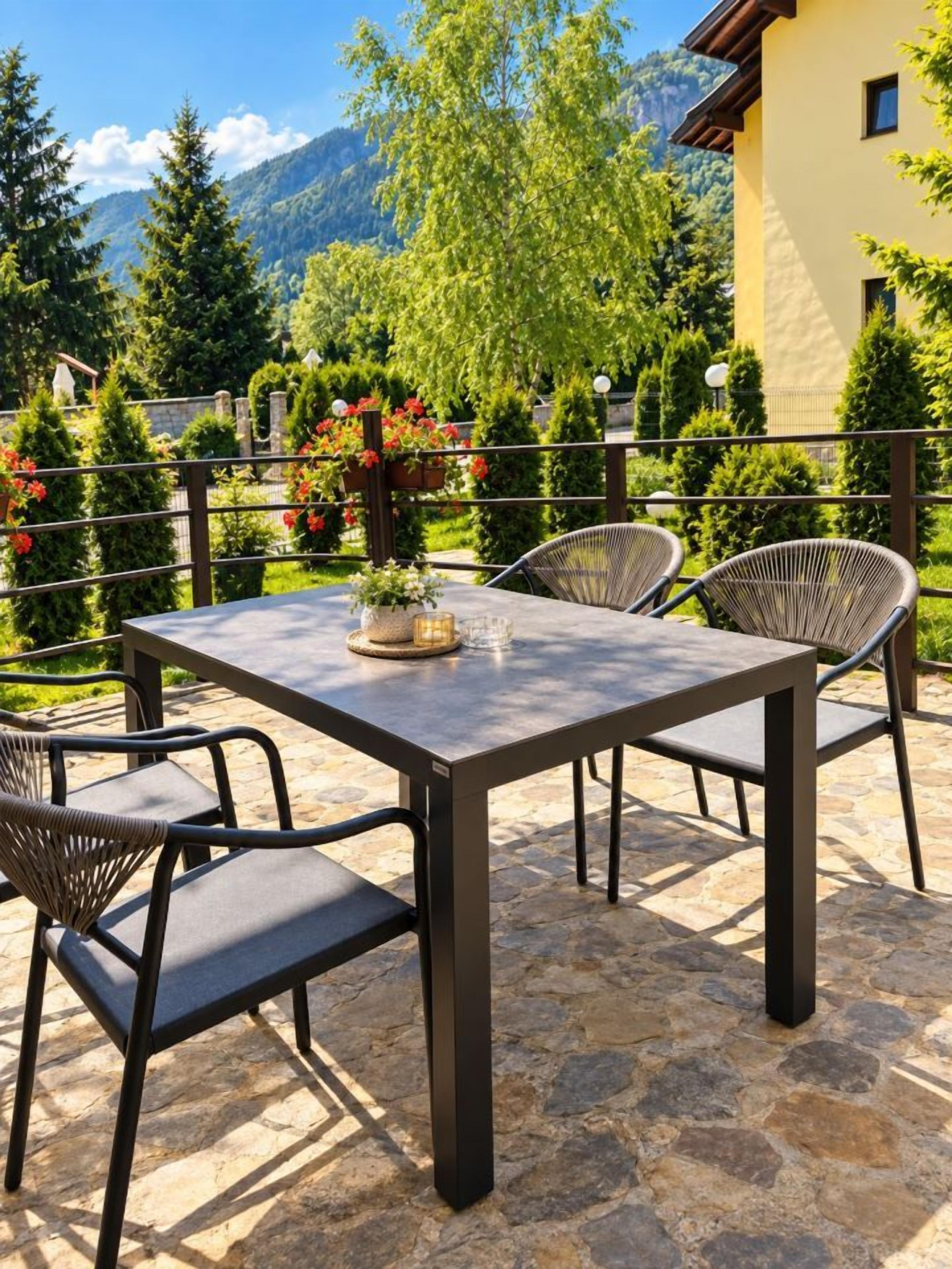 An outdoor patio with a table and chairs, surrounded by greenery and mountains in the background.