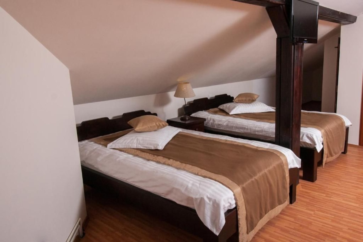 A hotel room with two beds, wooden headboards, a nightstand, and a lamp.