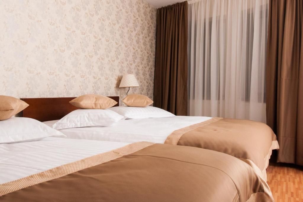 Habitación de hotel con dos camas, cabecero, lámpara y ventana con cortinas.