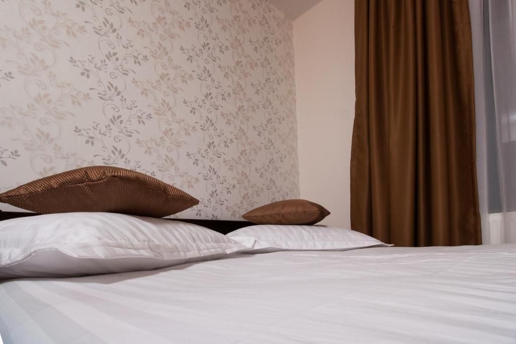 Una cama bien hecha con sábanas blancas y dos almohadas marrones.
