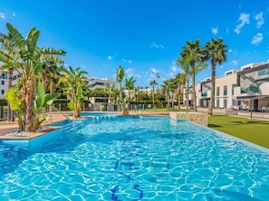 A swimming pool with clear blue water, surrounded by palm trees and modern buildings. - Spacious 3-bedroom apartment with AC in charming El Raso (el raso)