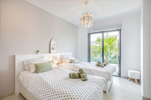 A modern bedroom with two beds, a large window with a view of palm trees, a decorative globe light, and a surfboard art piece. - Spacious 3-bedroom apartment with AC in charming El Raso (el raso)
