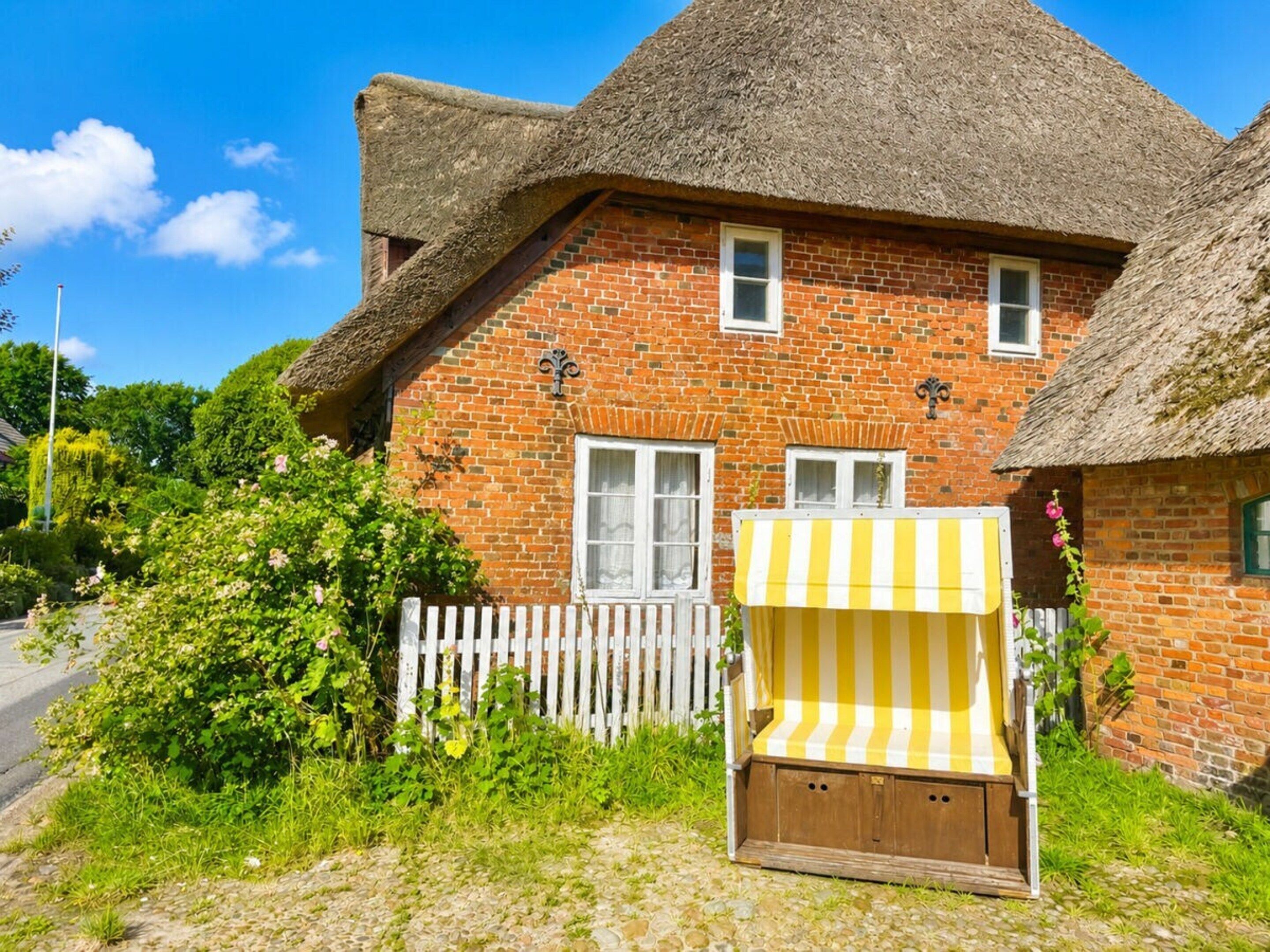 A brick house with a thatched roof, a white picket fence, and a yellow-striped awning.