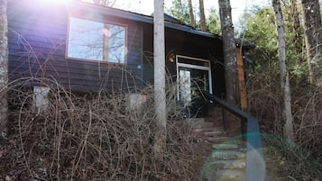 A cabin with a wooden exterior, a front door, and a staircase leading up to the entrance.