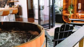 A wooden barrel-shaped hot tub with a metal railing in front, a dining area with chairs and a table, and a glass door leading to an outdoor space.