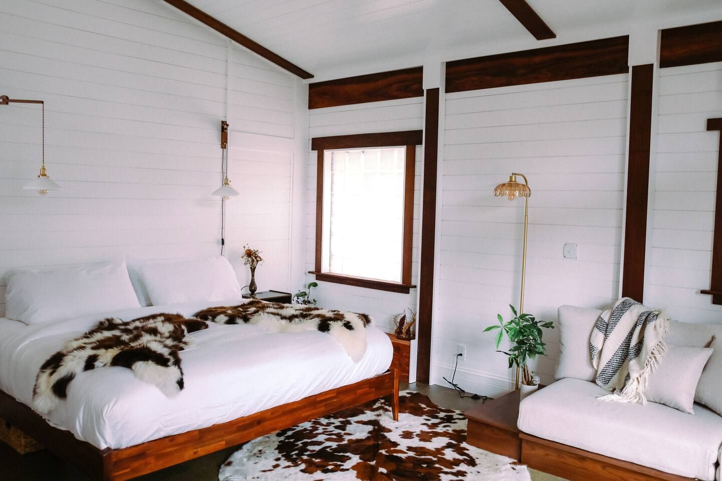 A room with a wooden bed, a white sofa, a cowhide rug, and a large window.