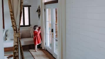 A room with a wooden floor, a sofa, a child in a red dress, and a window with curtains.