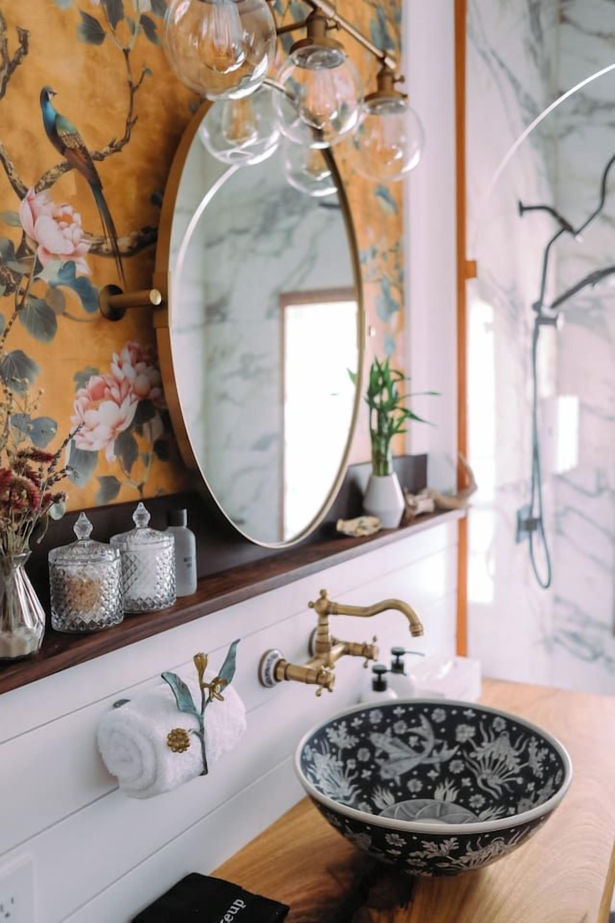A bathroom with a round mirror, a black and white floral bowl sink, and a wooden vanity.