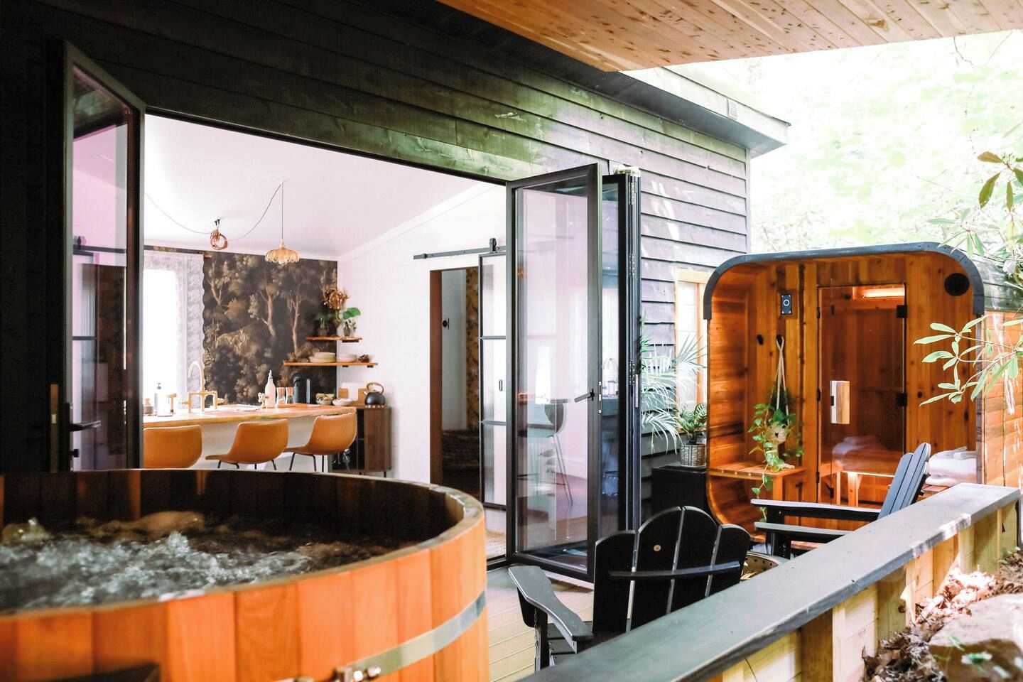 A modern outdoor dining area with a hot tub, wooden deck, and a glass-enclosed room with a dining table and chairs.