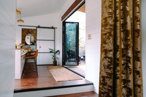 A modern interior with a wooden floor, a dining area with a chair and table, and a large window. - Dark City Solarium – Sauna + Hot Tub + Luxury (Black Mountain)