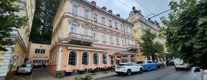 A multi-story building with a balcony, a restaurant named 'Villa Dancer' on the ground floor, and a parking area with several cars. - Family friendly 2 Bedroom 2 Bathroom with Balcony Apartment. Pet friendly (Marianske Lazne)