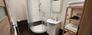 A bathroom with a glass-enclosed shower, a sink, and a wooden shelf with towels. - Family friendly 2 Bedroom 2 Bathroom with Balcony Apartment. Pet friendly (Marianske Lazne)