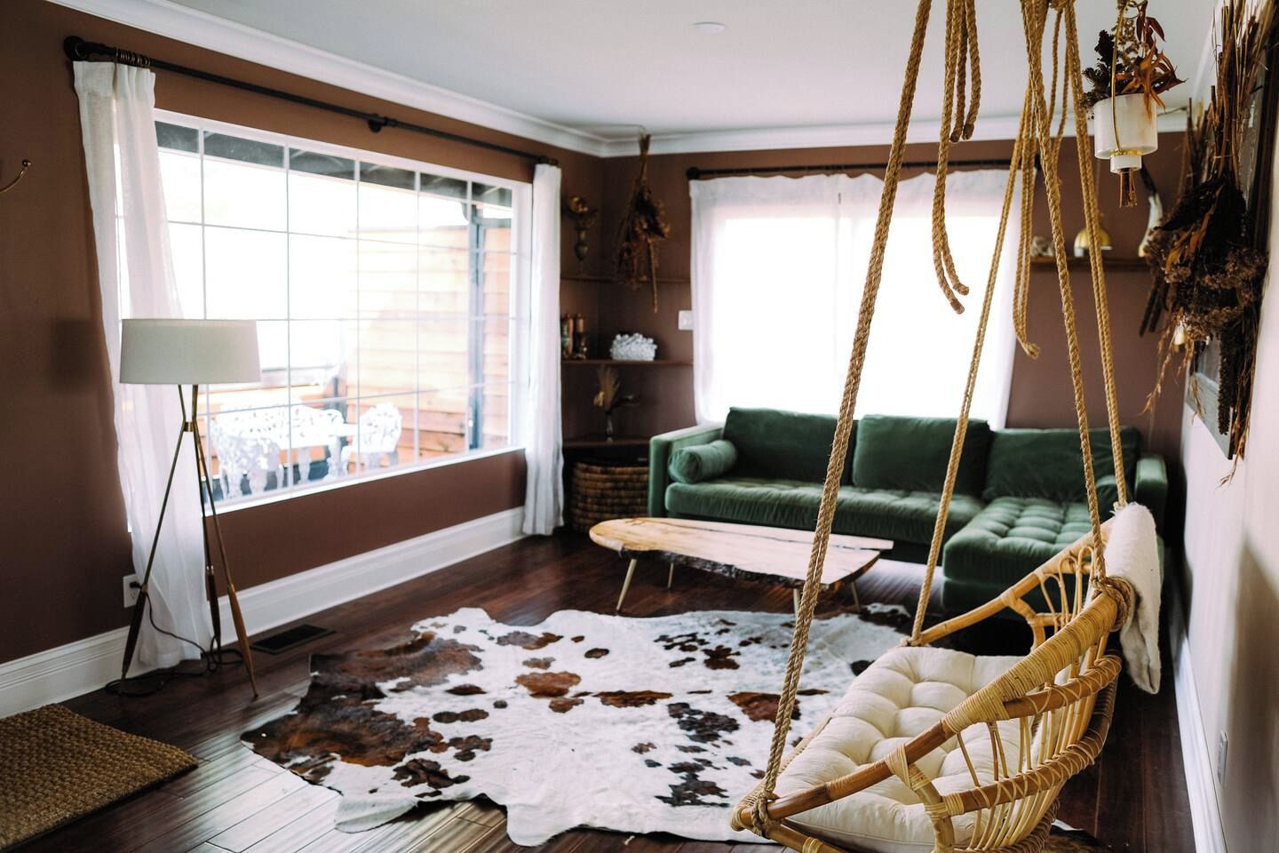 A living room with a hanging chair, a green sofa, a cowhide rug, and a floor lamp.