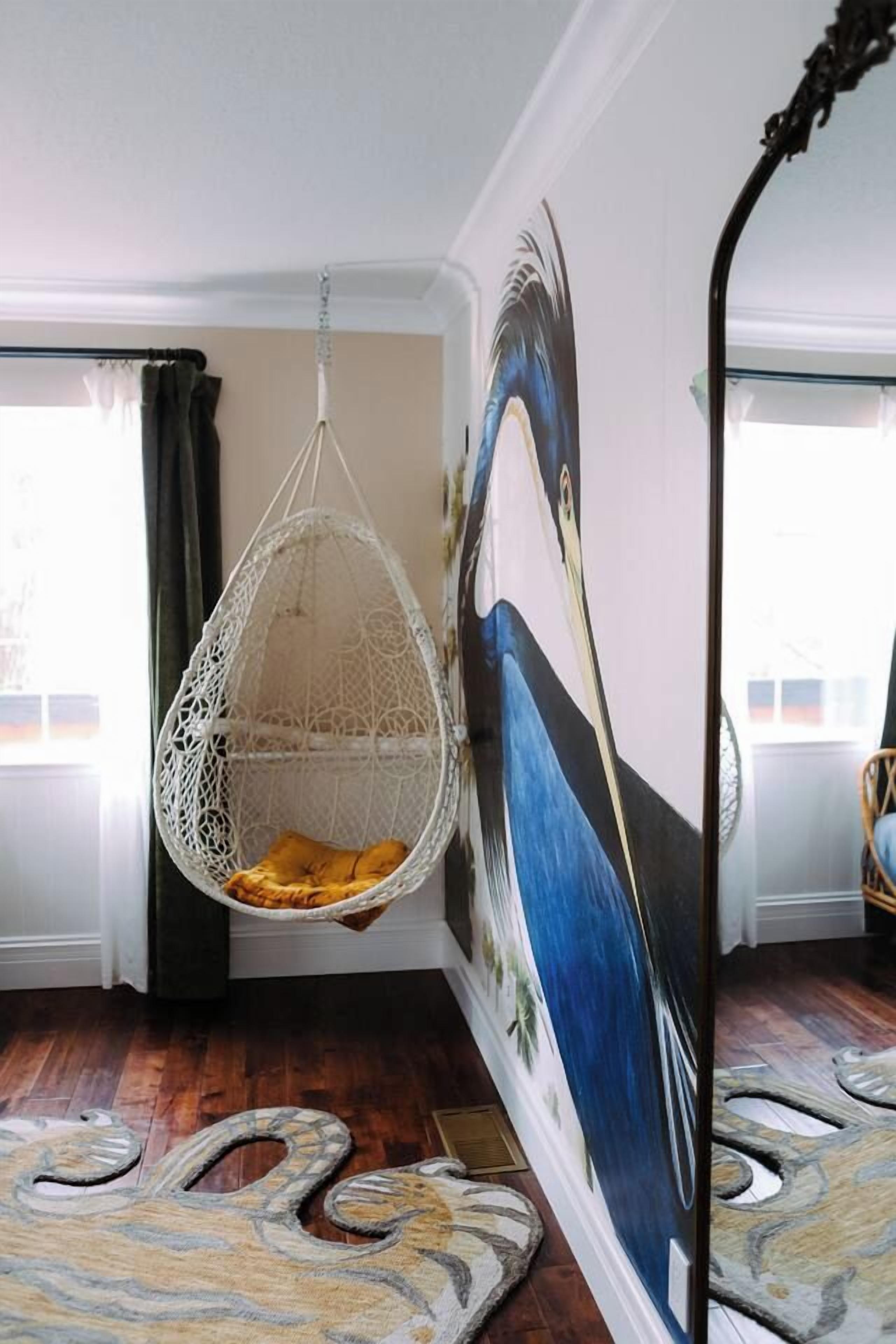 A room with a hanging chair, a large painting, and a patterned rug.