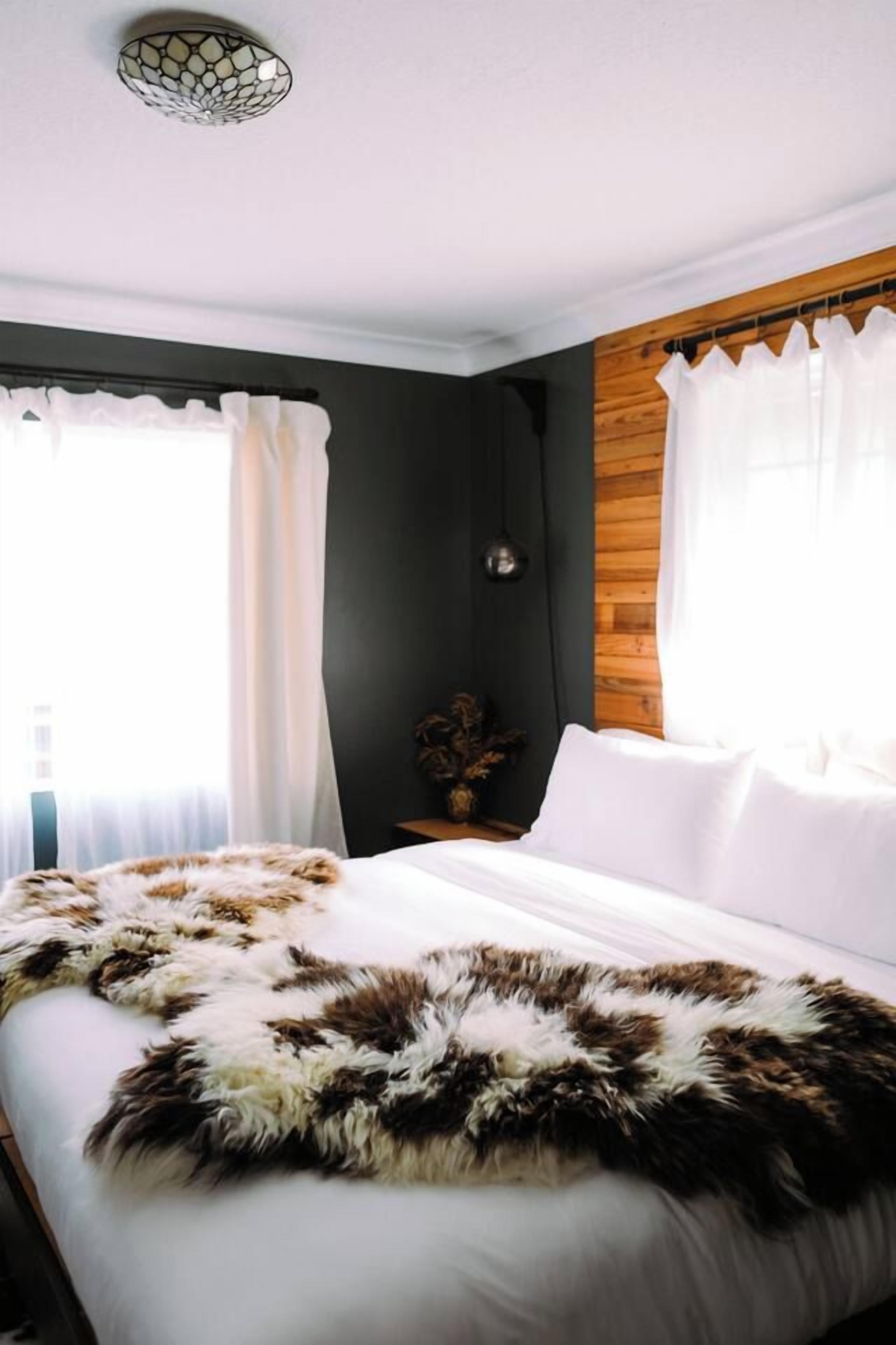 A bedroom with a bed, curtains, a wall-mounted lamp, and a window.