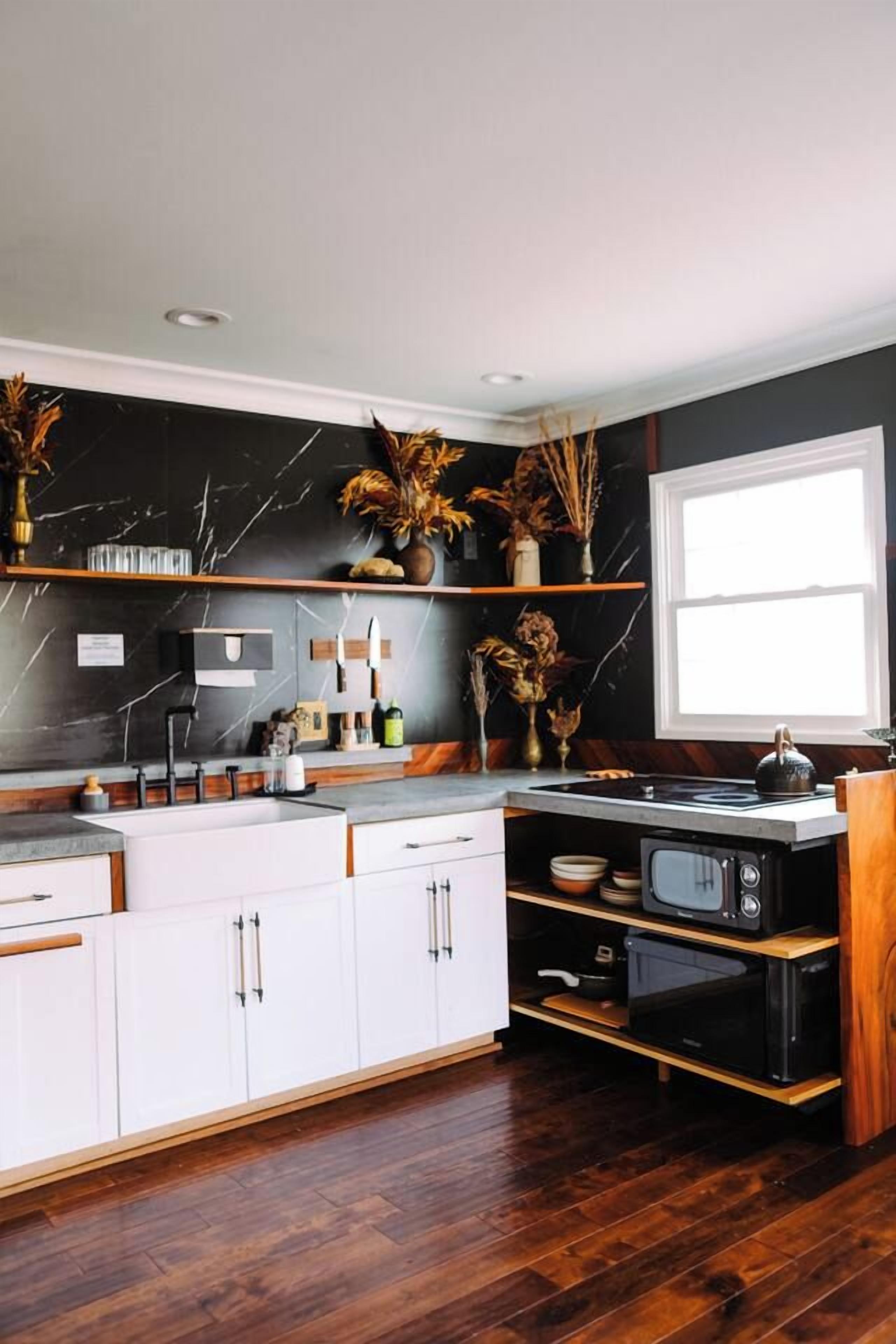 A modern kitchen with white cabinets, a black backsplash, and wooden flooring.