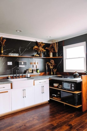Una cucina moderna con mobili bianchi, uno schienale nero e pavimento in legno.